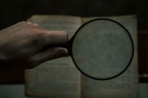 Hands holding a magnifying glass over printed documents